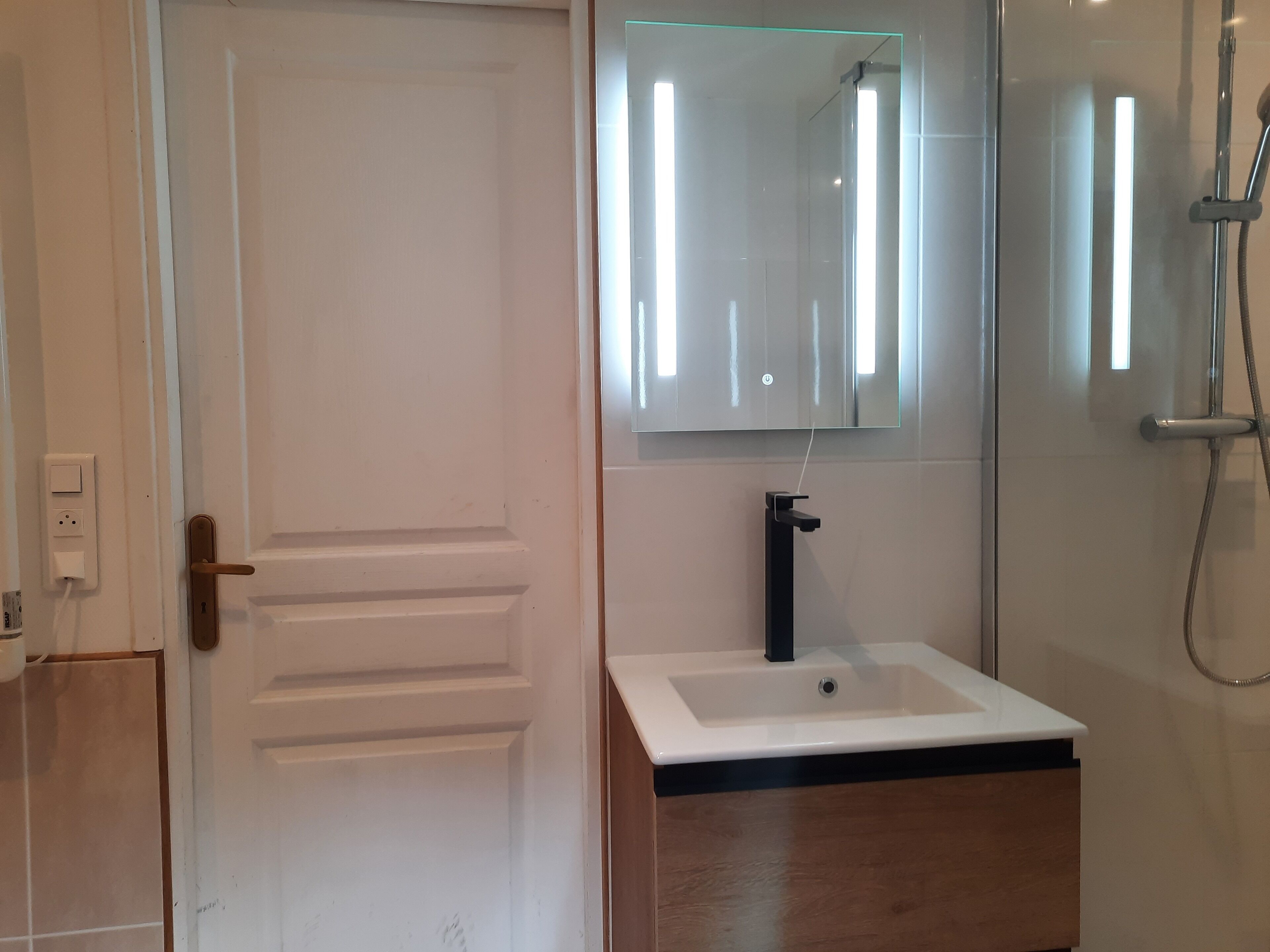 Une salle de bain avec une porte blanche, un lavabo surmonté d’un miroir et un espace douche.