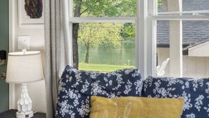 A bedroom with a window view of a lake, a bedside lamp, and a 'Welcome' pillow. - Hummingbird Hideway Peaceful Lake View Cottage (Rockaway Beach)