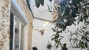 A small patio area with a stone wall, a sliding glass door, a white plastic chair, a small table, and a potted plant.