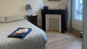 A bedroom with a bed, a fireplace, a mirror, and a window.