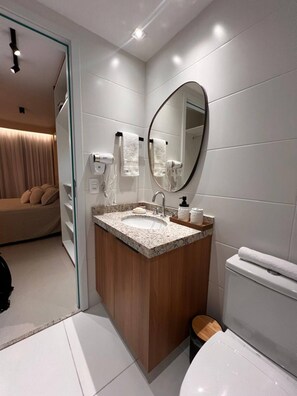 Een moderne badkamer met een wastafel op een granieten blad, een houten wastafelmeubel, een grote spiegel en een toilet.