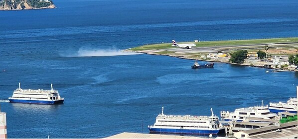 Un puerto con varios cruceros amarrados, un barco grande en primer plano y un avión en la pista al fondo.