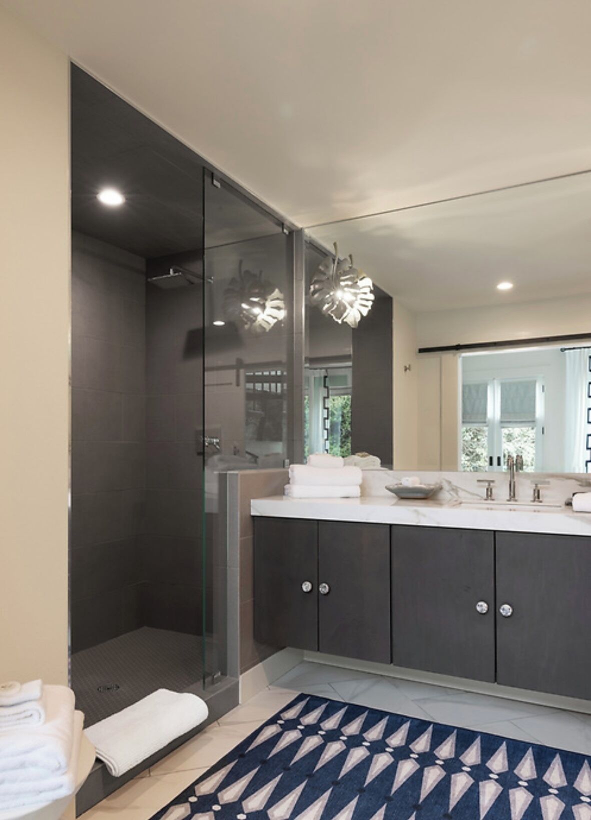 A modern bathroom with a glass shower enclosure, dark cabinetry, and a marble countertop.