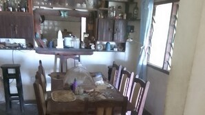 Un comedor con una mesa dispuesta para cuatro personas, rodeada de sillas de madera. Un ventanal grande proporciona luz natural y el piso es de baldosas.