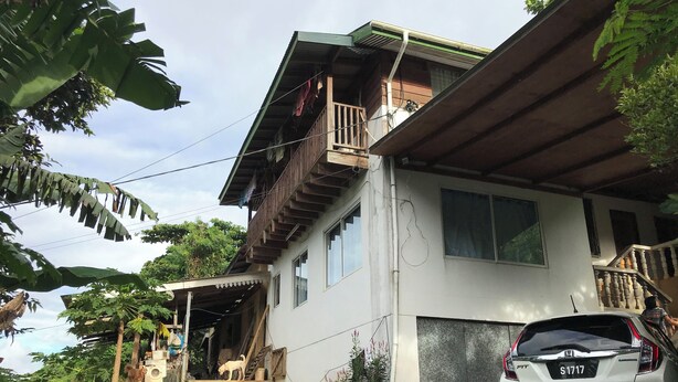 Una casa de dos pisos con un balcón, una escalera que lleva a la entrada y un coche aparcado.