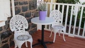 En terrasse med to hvide metalstole og et rundt bord med en lilla potte.