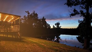 Un espace extérieur abrité, agrémenté de guirlandes lumineuses, un terrain herbeux et une étendue d’eau.