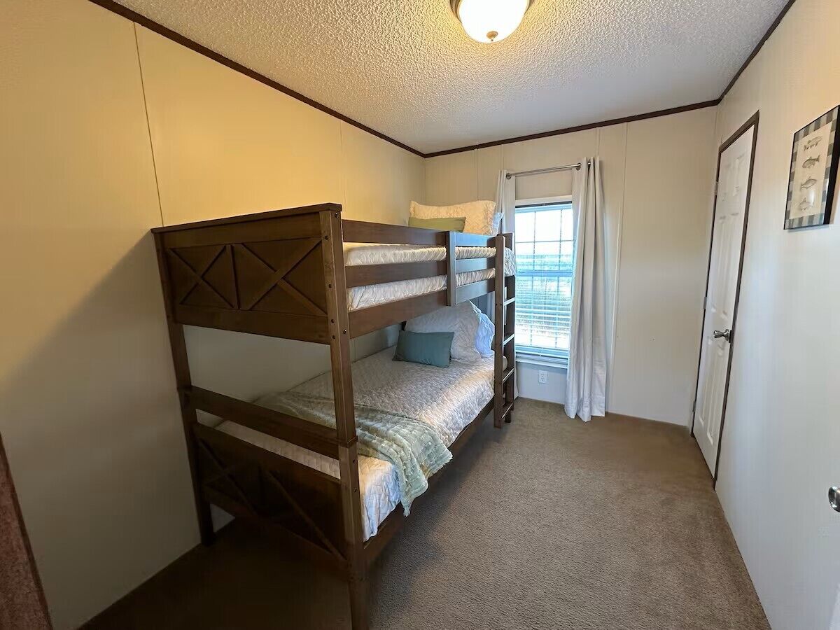 Una cama litera en una habitación con una puerta, una ventana con cortinas y una lámpara en el techo.