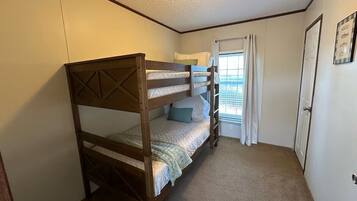 Una cama litera en una habitación con una puerta, una ventana con cortinas y una lámpara en el techo.
