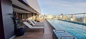 Pool på taget med liggestole og udsigt over byen.
