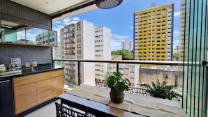 Eine moderne Küche mit einem großen Fenster, einem Balkon mit einer Pflanze und Blick auf umliegende Gebäude.