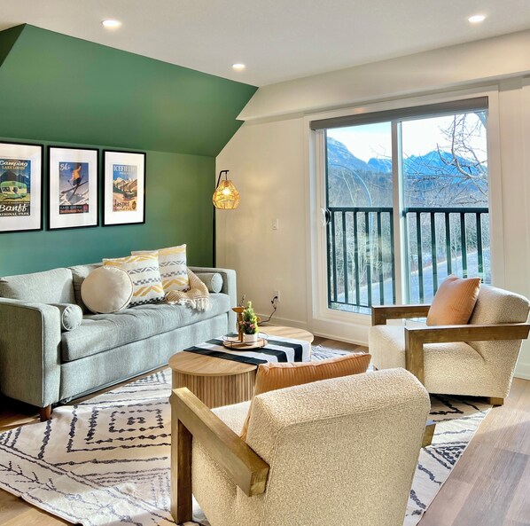 Un salon moderne avec un mur d’accent vert, une grande fenêtre donnant sur les montagnes, un canapé, une table basse et un fauteuil.