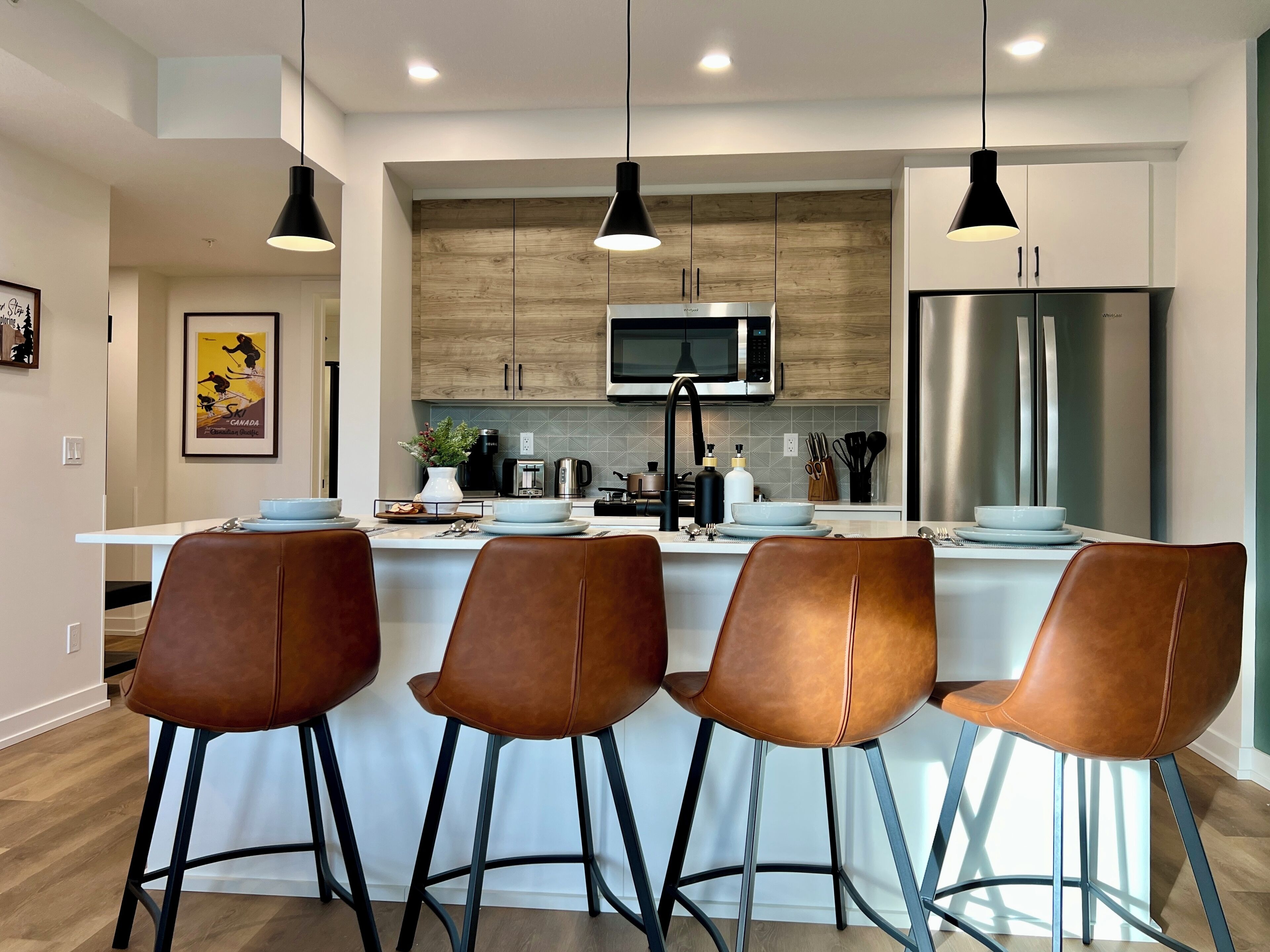 Una cocina moderna con una isla central, electrodomésticos de acero inoxidable y taburetes de cuero marrón.
