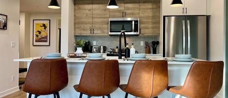 Una cocina moderna con una isla central, electrodomésticos de acero inoxidable y taburetes de cuero marrón.