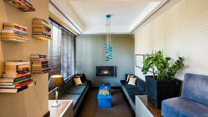 A modern living room with a fireplace, bookshelves, a blue coffee table, and a large plant. - The Athens Gate Hotel (Athens)