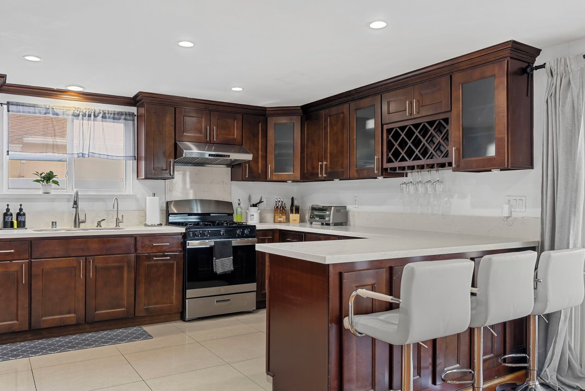 A modern kitchen with dark wooden cabinets, a stainless steel range, and a bar area with white stools.