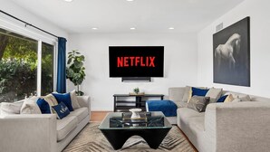 Ein modernes Wohnzimmer mit zwei Sofas, einem Couchtisch und einem an der Wand montierten Fernseher, der "NETFLIX" anzeigt.