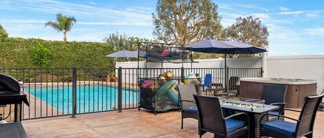 An outdoor patio with a pool, a table with chairs, and a hot tub.