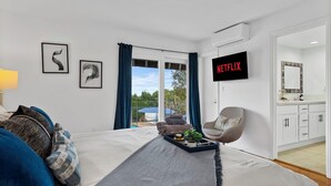 Ein modernes Hotelzimmer mit Bett, Fernseher mit 'NETFLIX', Blick ins Freie und einem Balkon mit einem blauen Sonnenschirm.