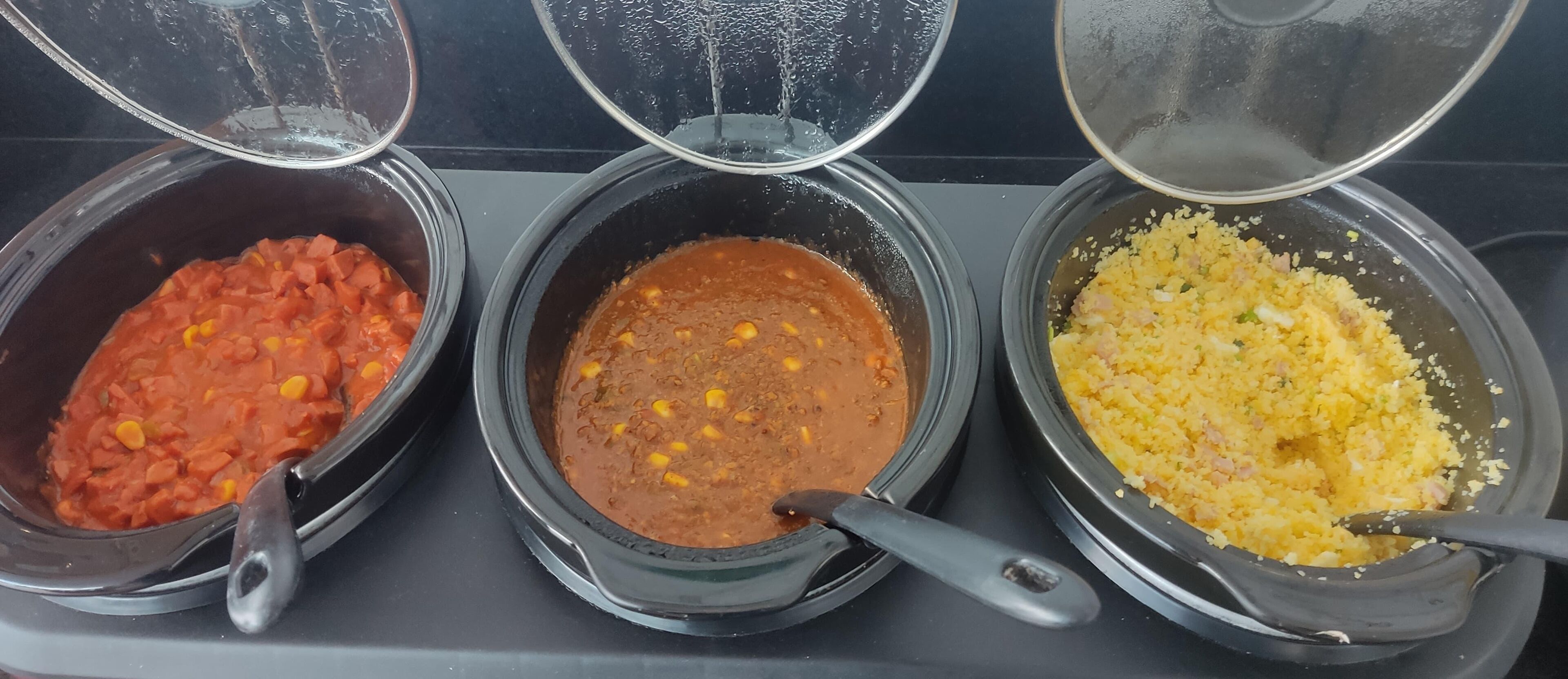 Three black pots on a stove with lids, containing different food items.
