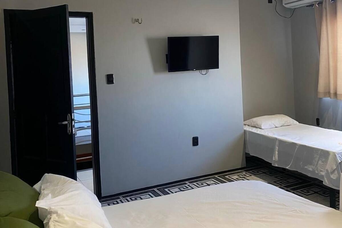 A hotel room with a bed, a green sofa, a TV mounted on the wall, and an air conditioning unit.