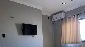 Une chambre d’hôtel équipée d’un lit, d’un téléviseur fixé au mur, d’un appareil de climatisation et d’une fenêtre avec des rideaux.