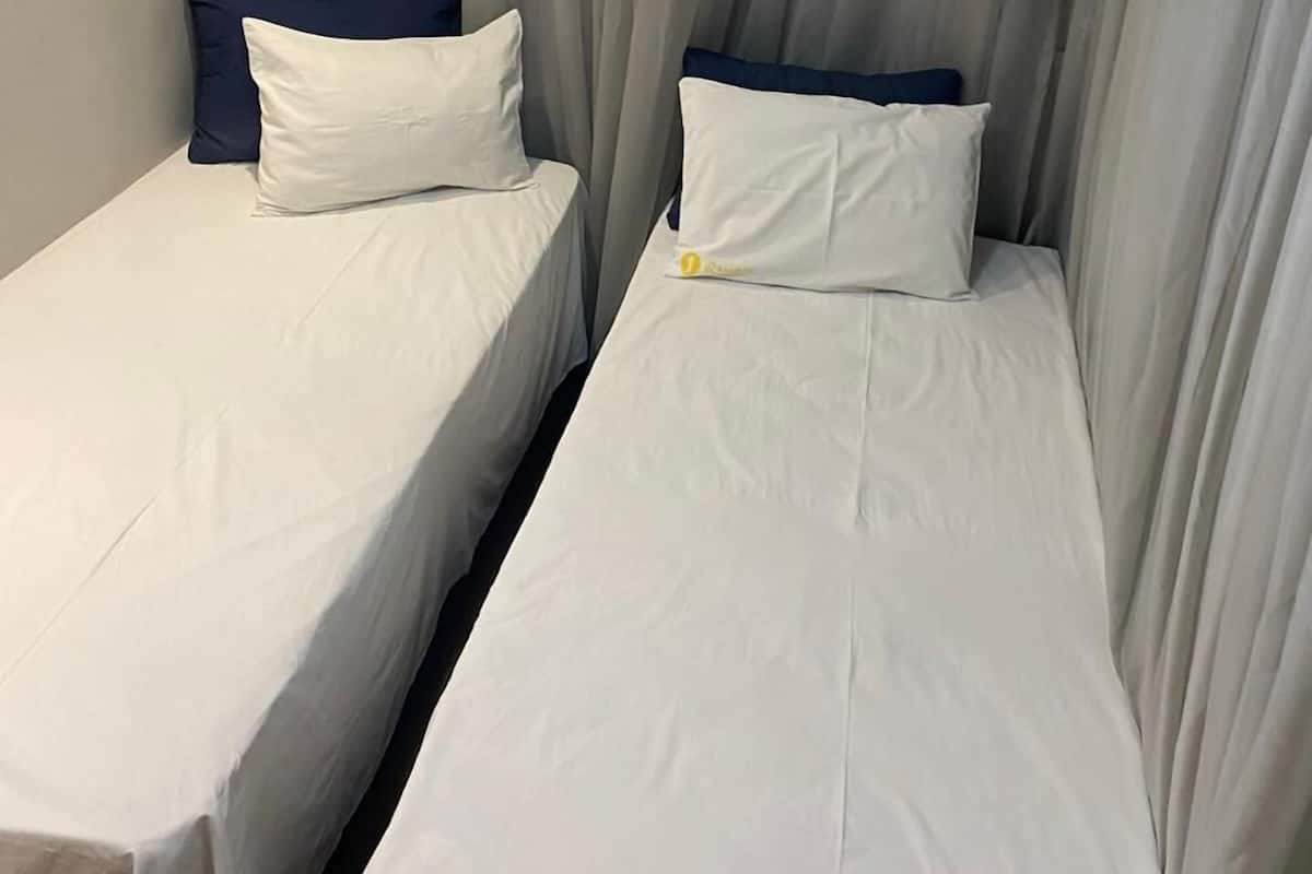 Two single beds with white linens and dark blue headboards, separated by a curtain.