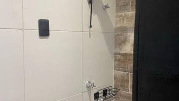 Un baño con paredes de azulejos blancos, una ducha con grifo negro y un estante pequeño con artículos de aseo.