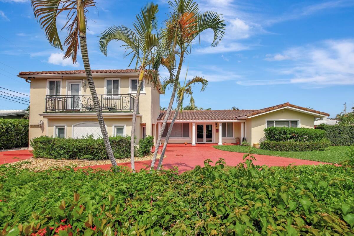 A two-story building with a red driveway, surrounded by greenery and palm trees.