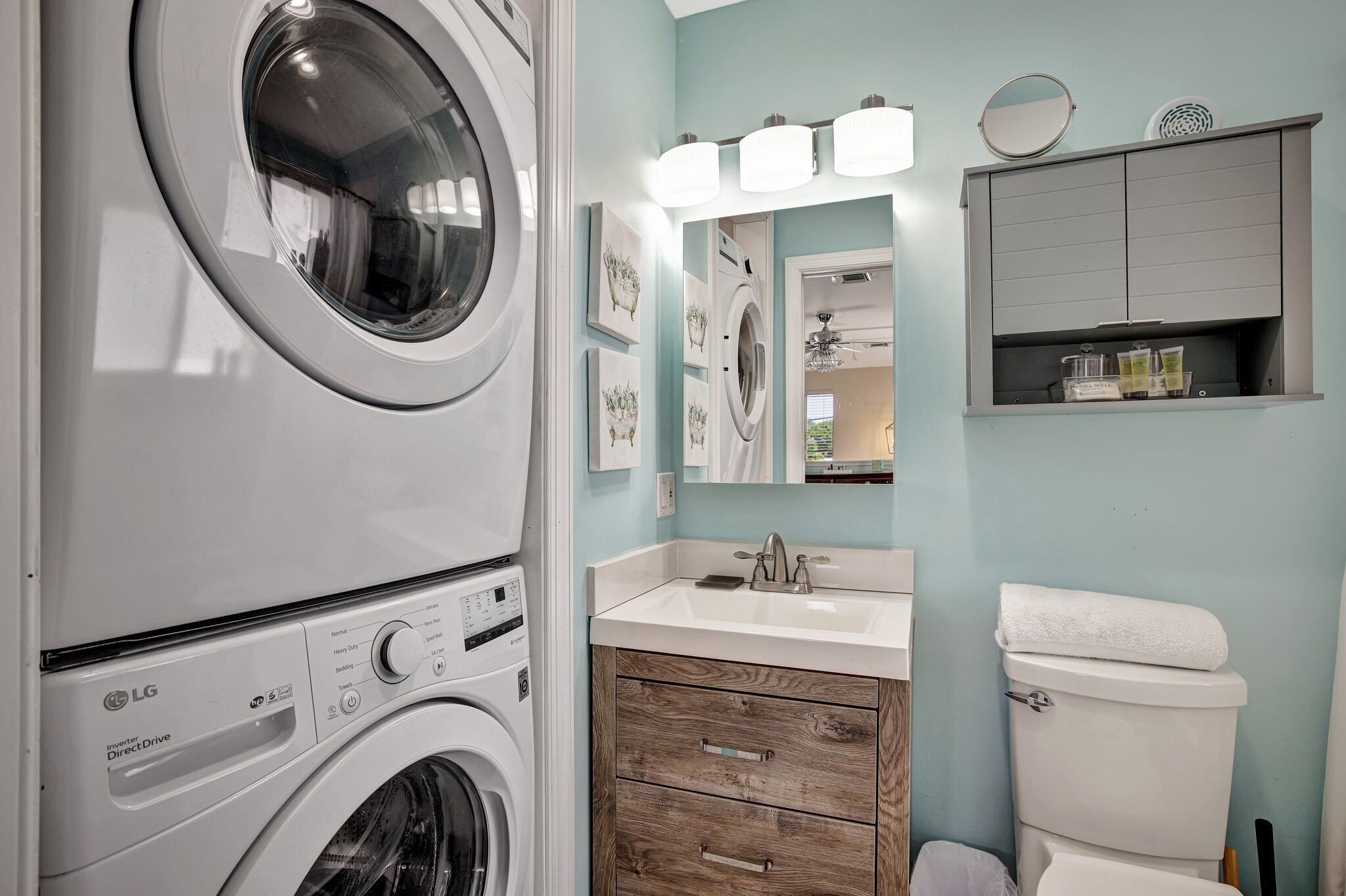 A laundry area with stacked washing machines, a wooden cabinet, a sink with a mirror, and a toilet.