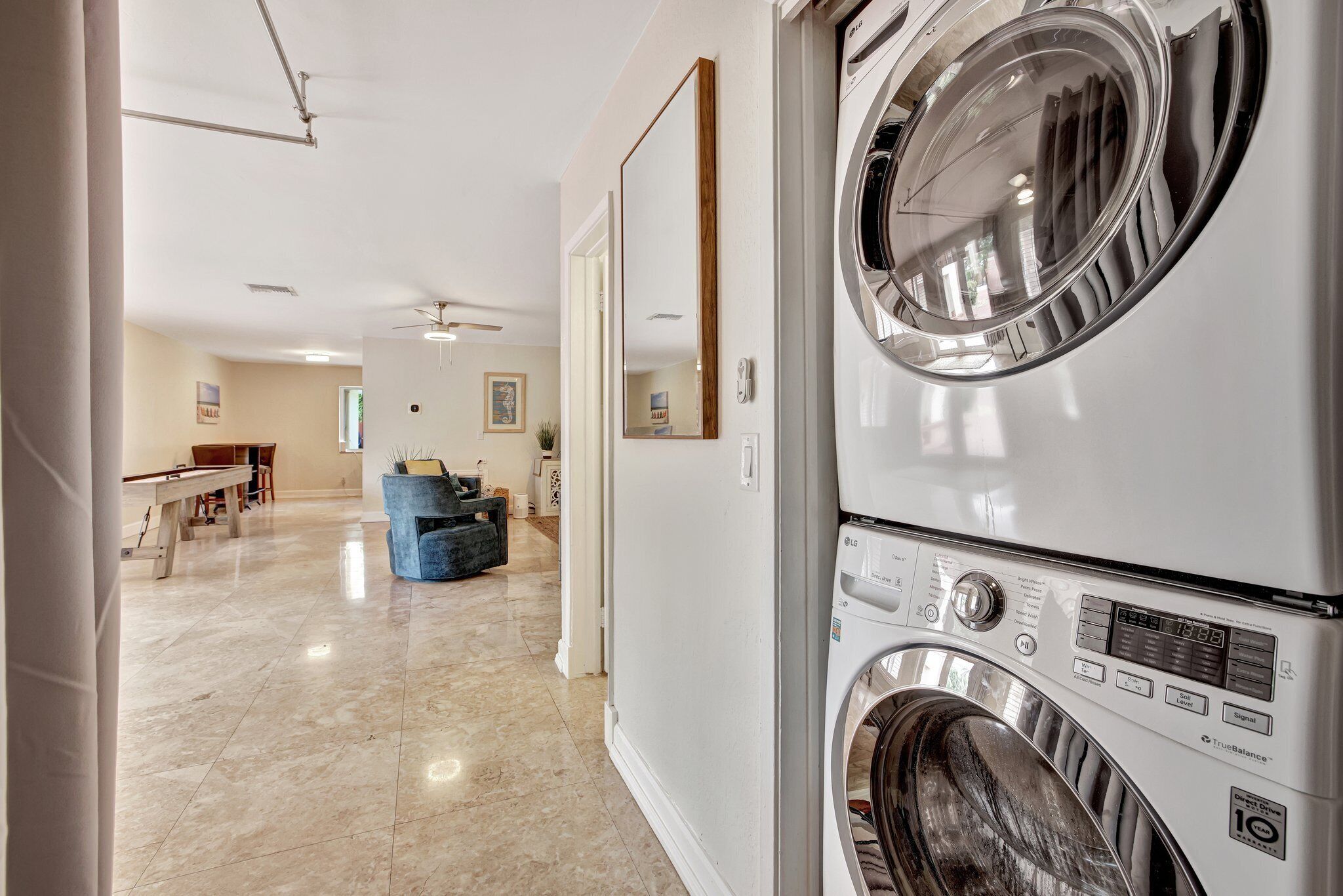 A laundry area with stacked washers and dryers, a ceiling fan, and a hallway leading to a dining area.