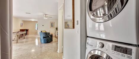 A laundry area with stacked washers and dryers, a ceiling fan, and a hallway leading to a dining area.