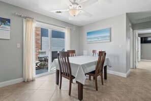 Un comedor con una mesa dispuesta para cuatro personas, un ventilador de techo y vistas a un patio exterior a través de un ventanal.