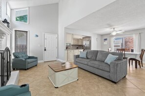 A spacious living room with a grey sofa, a coffee table, and a dining area with a table and chairs. - Charming 3BR Beach House w/ Yard & Grill ☀️ (North Myrtle Beach)