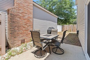 Un patio al aire libre con una mesa, sillas, una parrilla y un muro de ladrillo.
