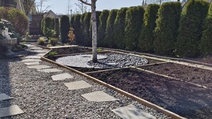 Un jardín con un camino de grava, un parterre circular y una estatua.