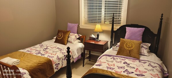 Une chambre avec deux lits, chacun recouvert d’une couvre-lit à motifs floraux et agrémenté d’oreillers assortis. Une table de chevet avec une lampe se trouve entre les deux lits.