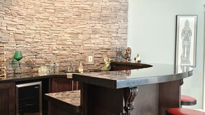 Una zona de bar con pared de piedra, un lavabo y encimera con varios objetos.