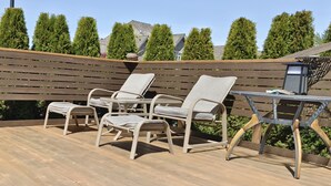 Una terraza de madera con mobiliario de mimbre, incluyendo sillas y una mesa, y un poste de luz de metal.