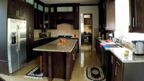 Una cocina amplia con armarios de madera oscura, una isla central, electrodomésticos de acero inoxidable y un amplio ventanal que proporciona luz natural.