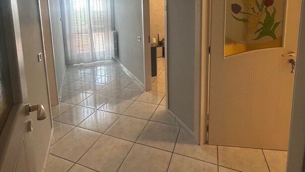 A hallway with tiled flooring, a door with a floral design, and a view into a room with a bed and curtains. - Safe Refuge (Macerata Campania)