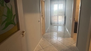 A hallway with tiled flooring, white doors, and a view of a room with a window and curtains. - Safe Refuge (Macerata Campania)