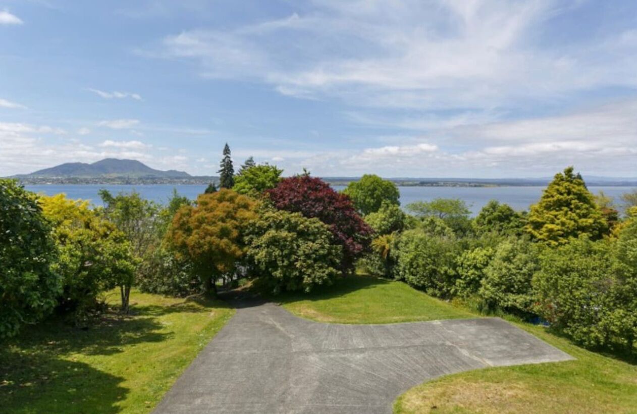 A paved driveway leading to a grassy area with trees and a view of a body of water and distant mountains.