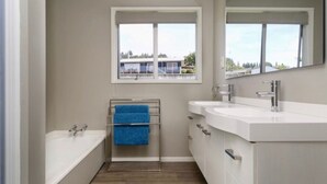 A modern bathroom with a bathtub, a sink, and a window. - Acacia Bay  - Lake and Mountain Views (Taupō)