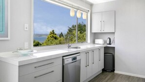 A modern kitchen with a large window, stainless steel appliances, and a view of greenery. - Acacia Bay  - Lake and Mountain Views (Taupō)
