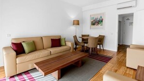 A living room with a sofa, coffee table, and chairs. There is a dining table with chairs, a lamp, and a painting on the wall. - Vilamoura Garden Hotel (Vilamoura)