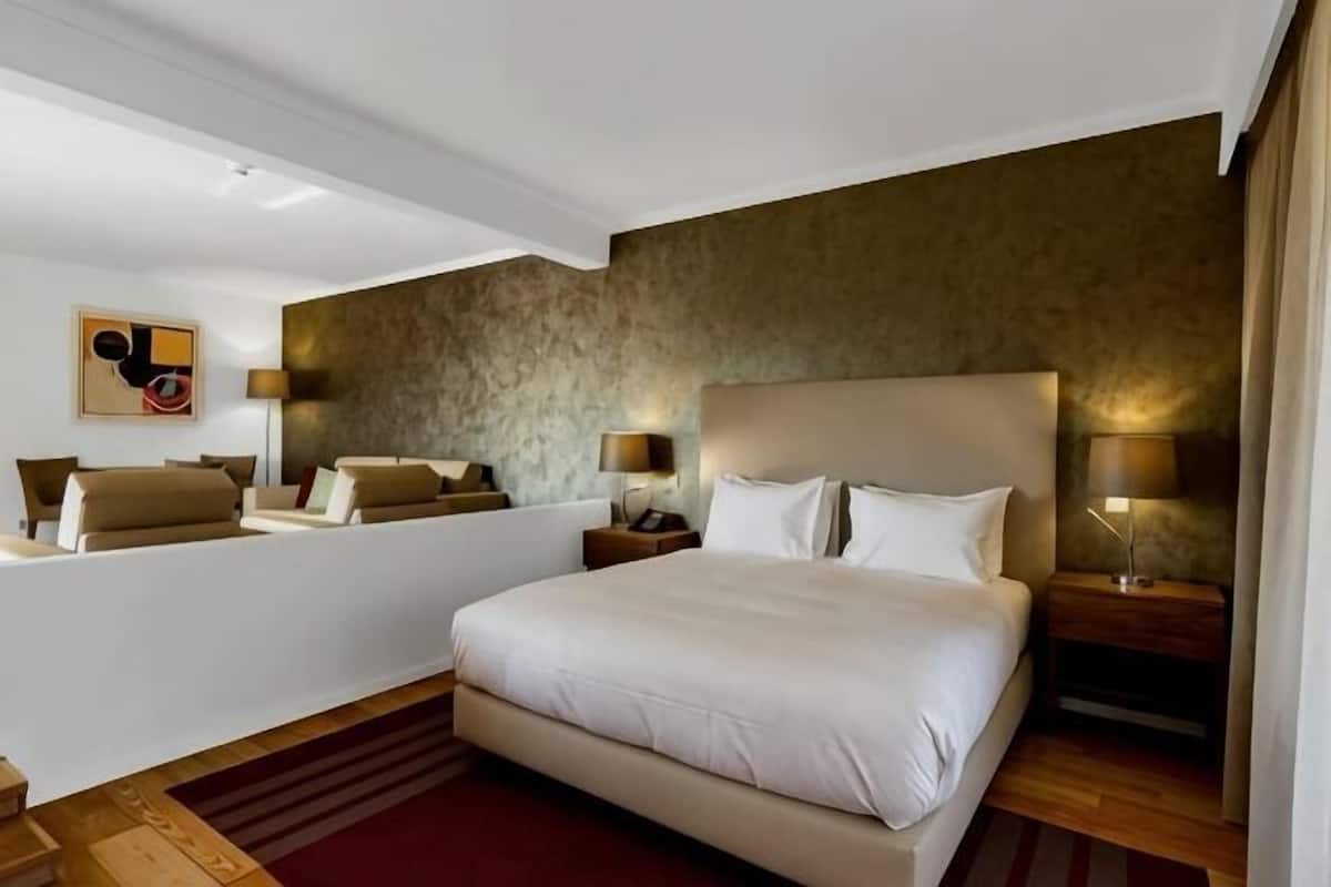 A hotel room with a large bed, bedside tables, a mirror, and a wall-mounted artwork.