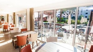 A modern hotel lobby with glass walls, a pool area visible through the windows, and a variety of seating arrangements. - Vilamoura Garden Hotel (Vilamoura)