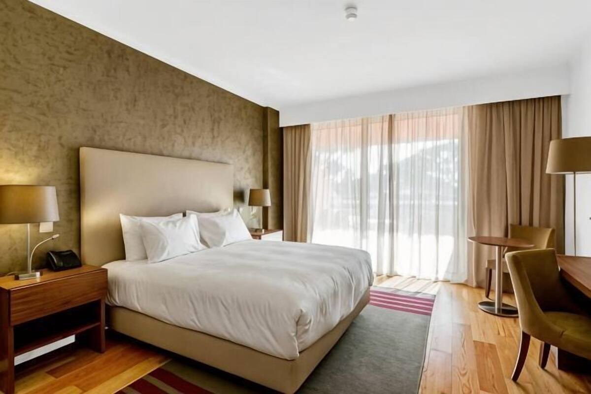 A hotel room with a large bed, bedside tables with lamps, a desk, and a chair.