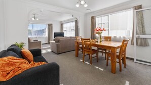 A modern living room with a sofa, dining table, and chairs, a TV, and large windows.